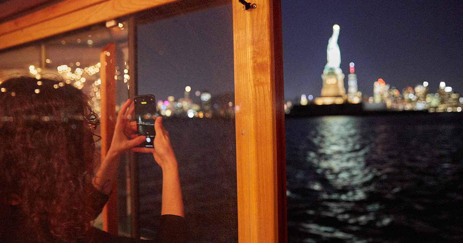 Person photographing Statue of Liberty from a boat at night.