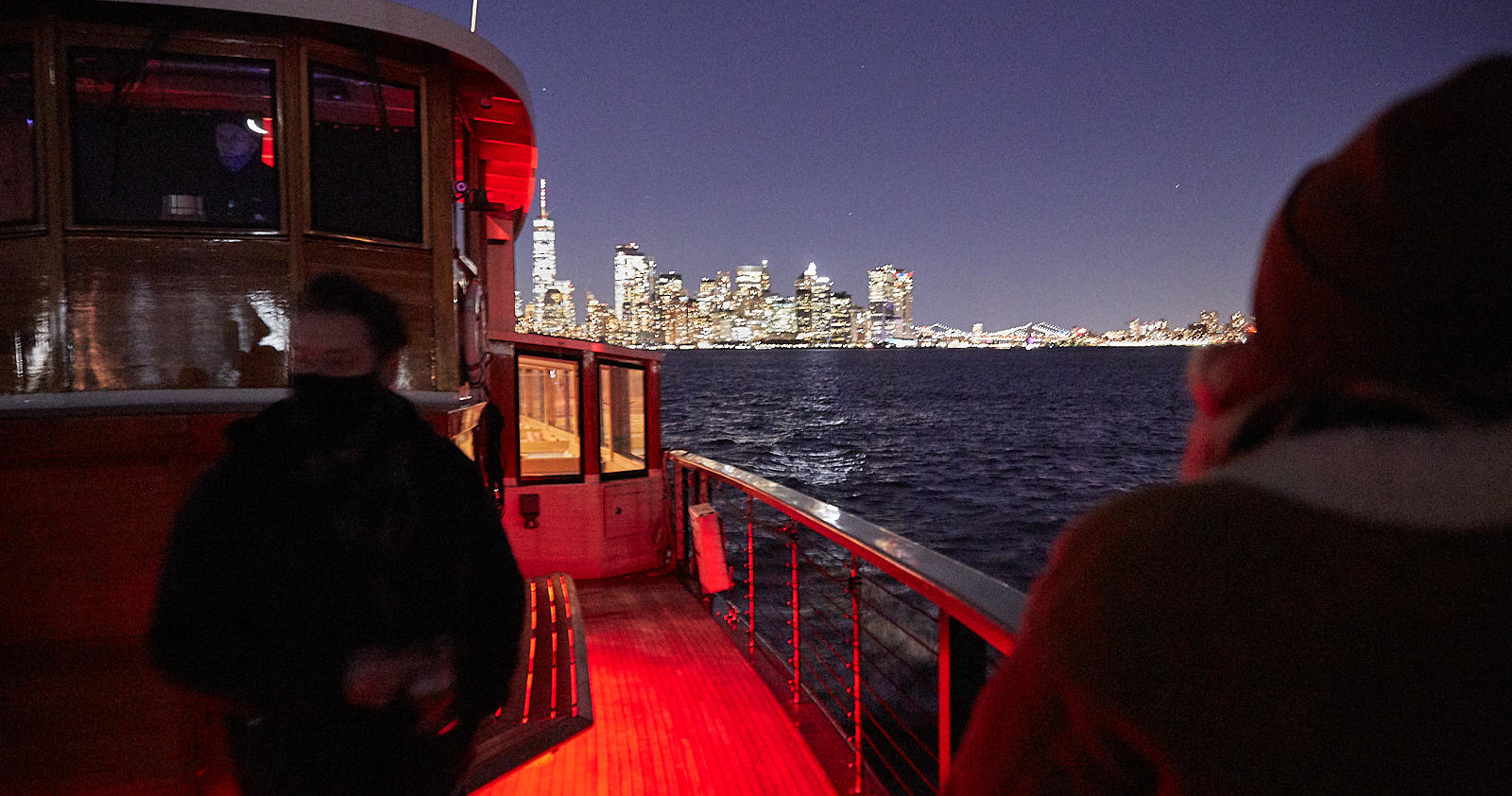 Two people on a boat at night, city skyline in the background.