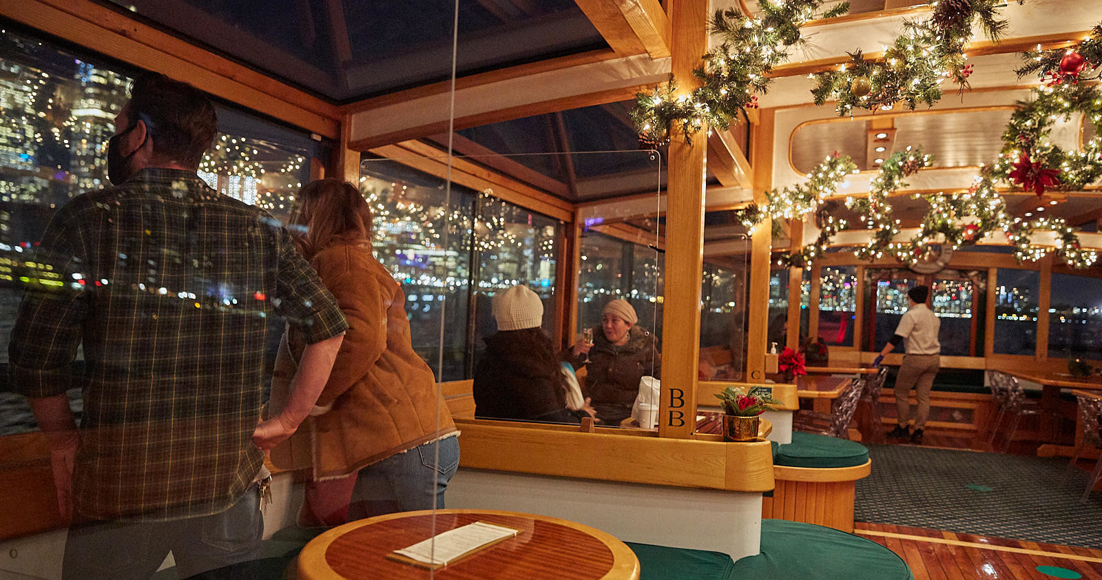 People inside a decorated boat with holiday lights and garlands, viewing city lights.