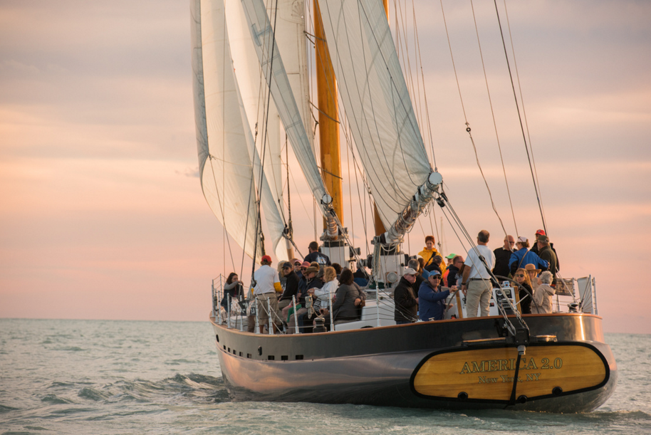 A large sailboat with many people onboard sailing at sunset.