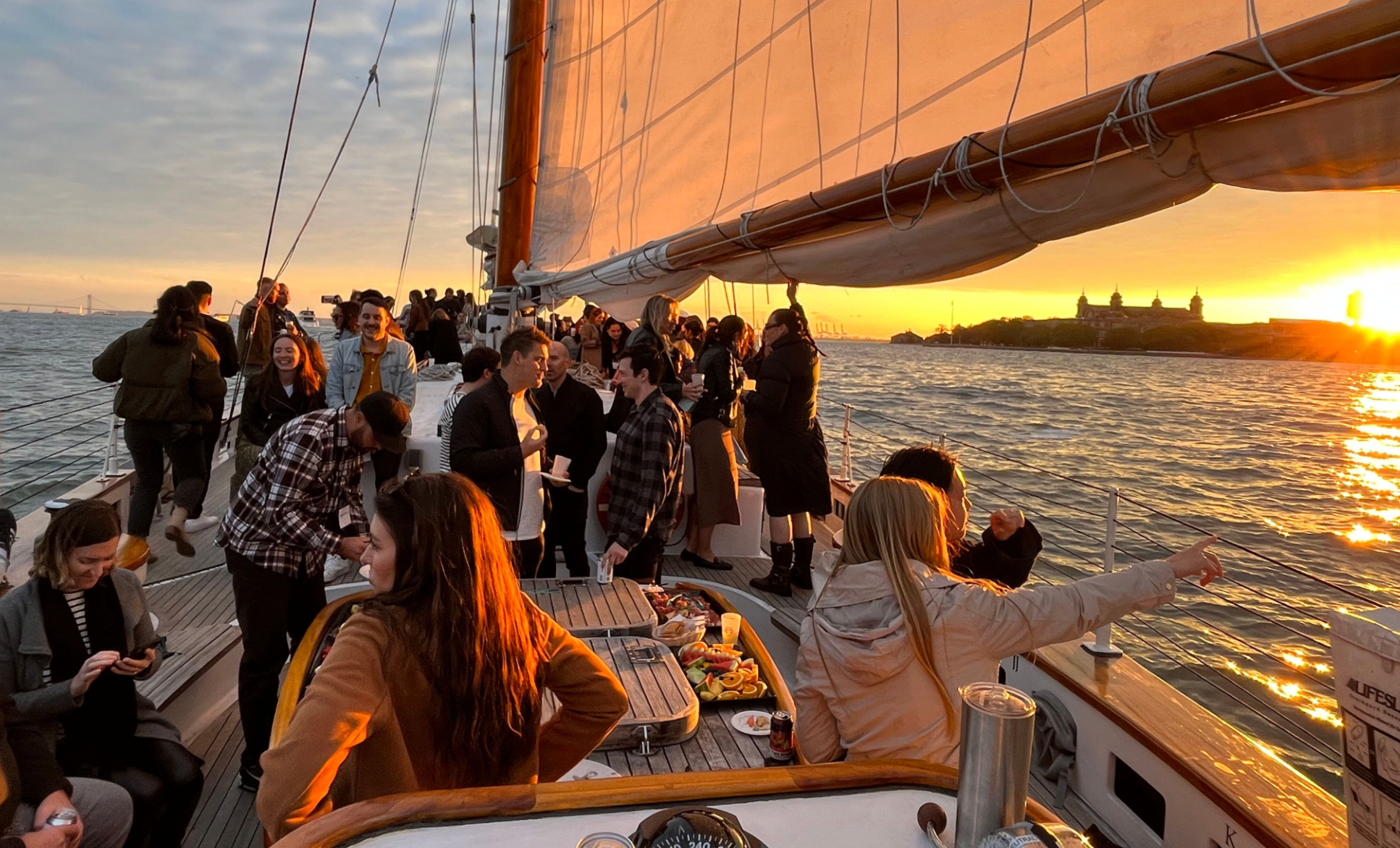 Group of people enjoying a sunset boat party with food on deck.