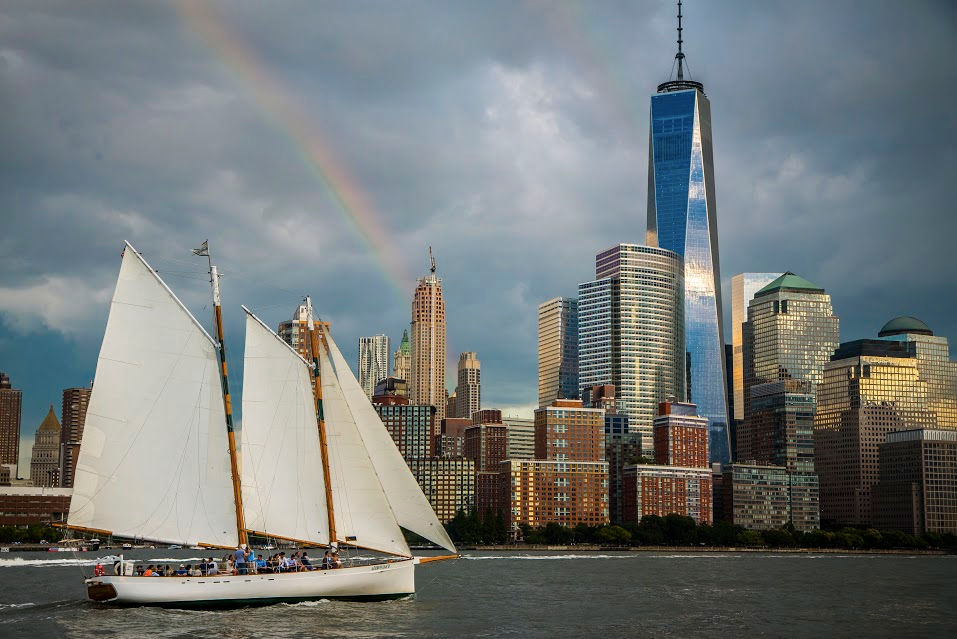 Sailboat on water with skyscrapers and a rainbow in the background.