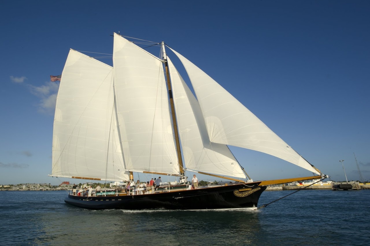 Large sailboat with three white sails on open water under clear blue sky.