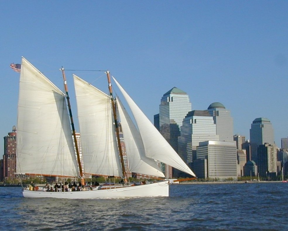 Sailing ship in harbor with city skyline in background.