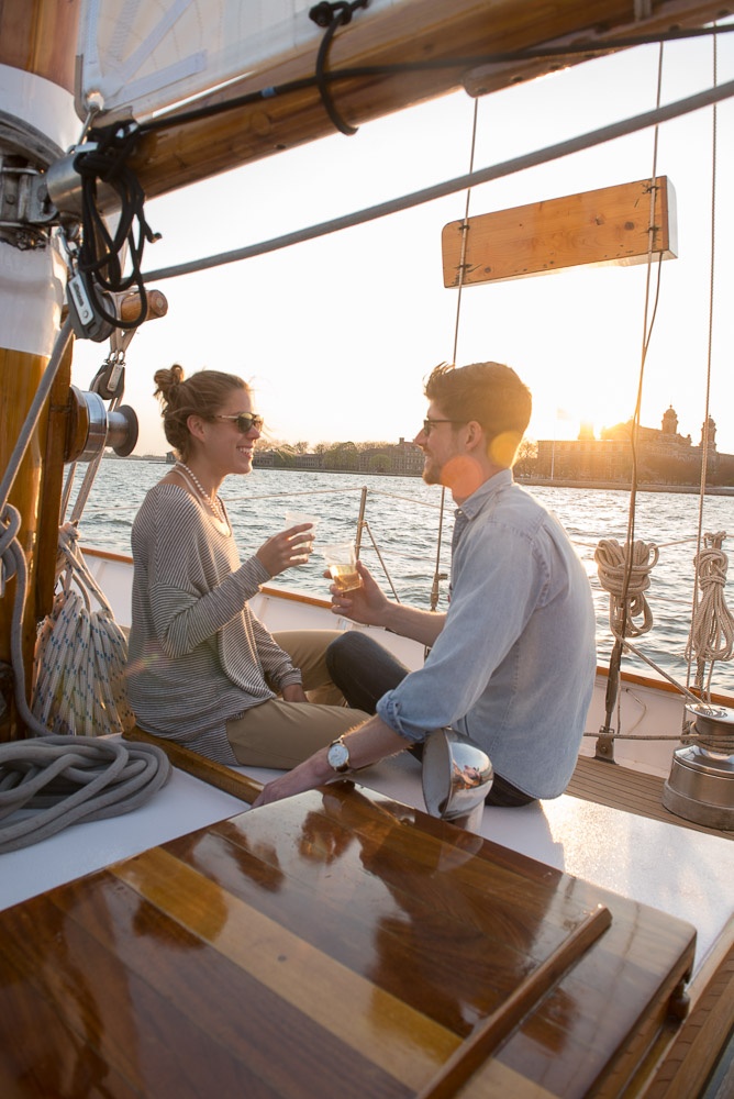 Two people sitting on a sailboat, enjoying drinks at sunset.