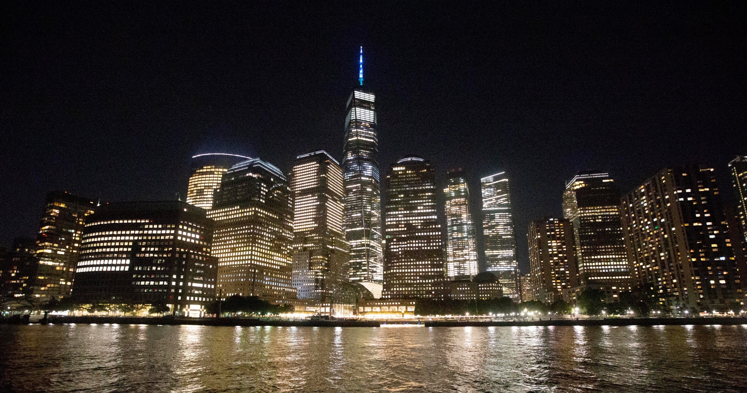 Night view of city skyline with illuminated skyscrapers and reflections on the water.