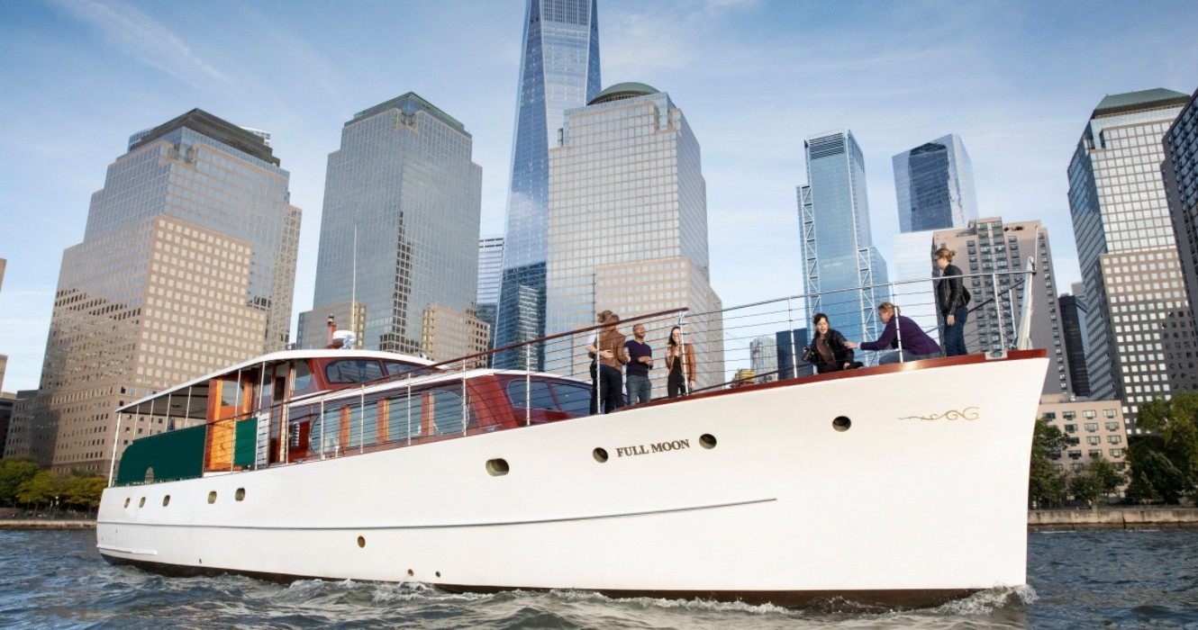 People on a white yacht in a city harbor with tall buildings in the background.