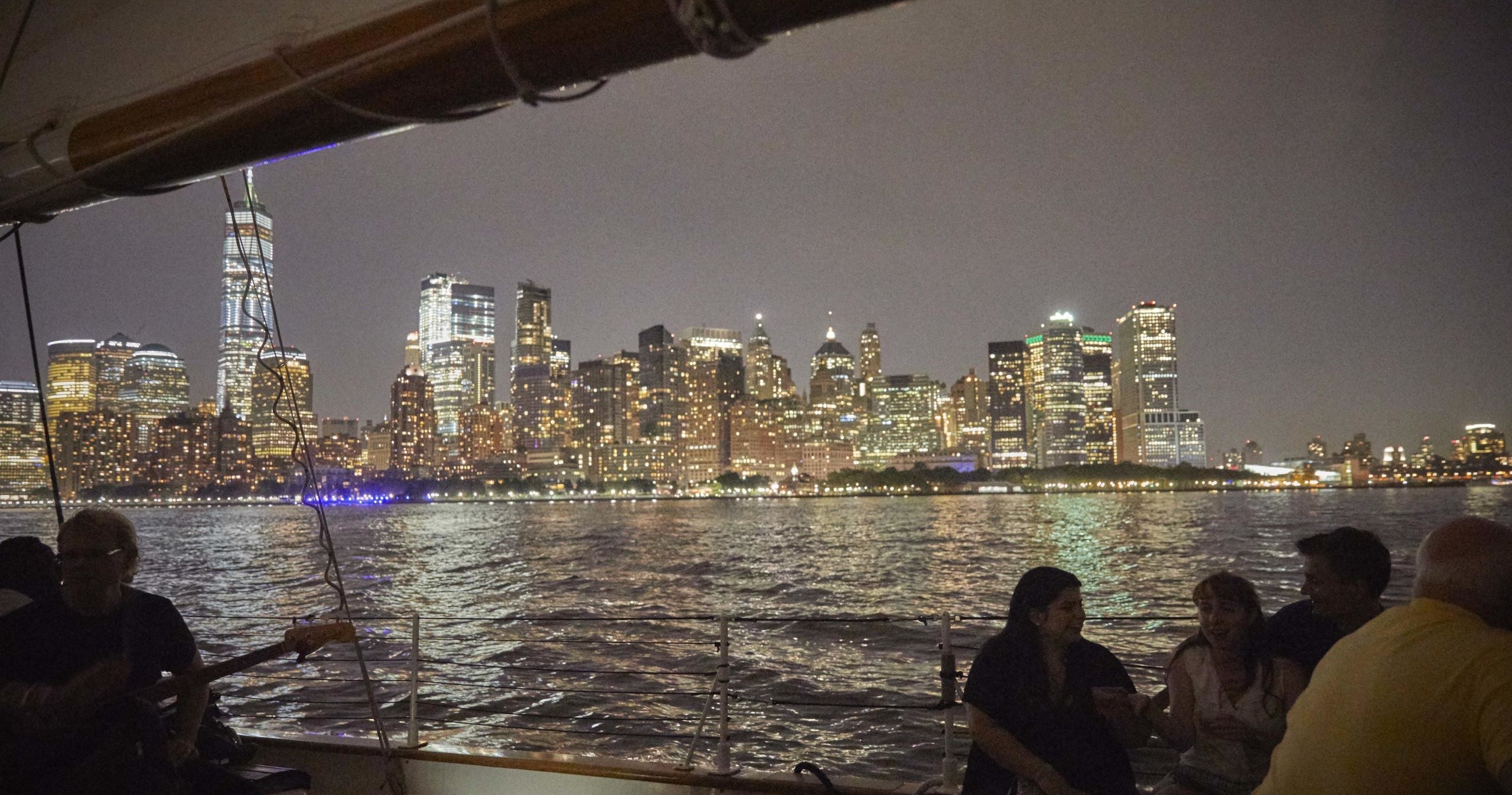 People on a boat view illuminated city skyline across water at night.