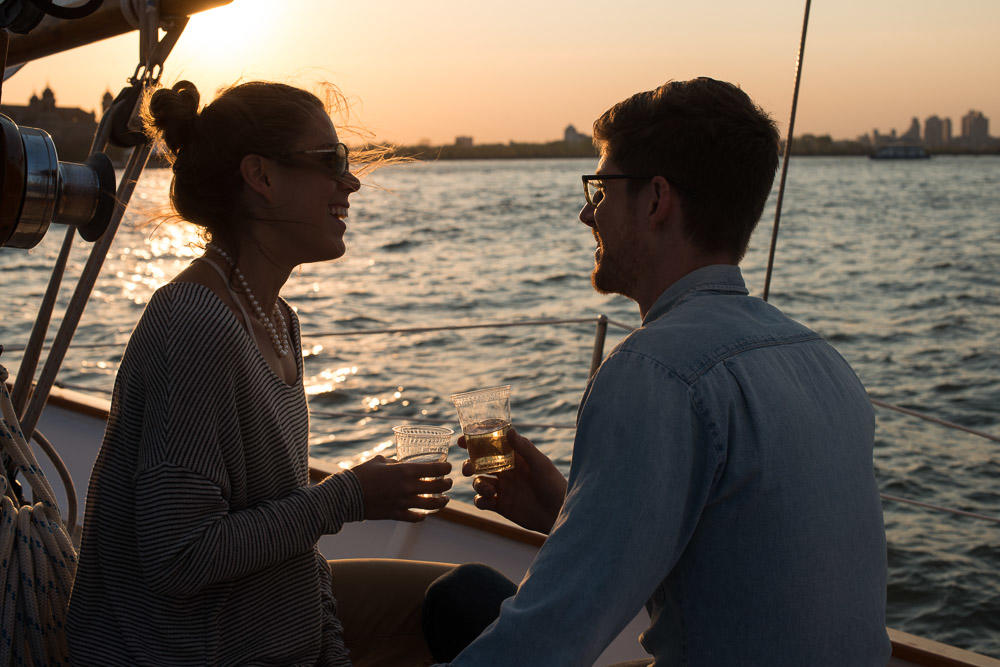 Couple on a boat at sunset, smiling and holding drinks.