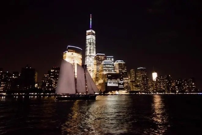 Night view of city skyline with sailboat in foreground and lit skyscrapers.