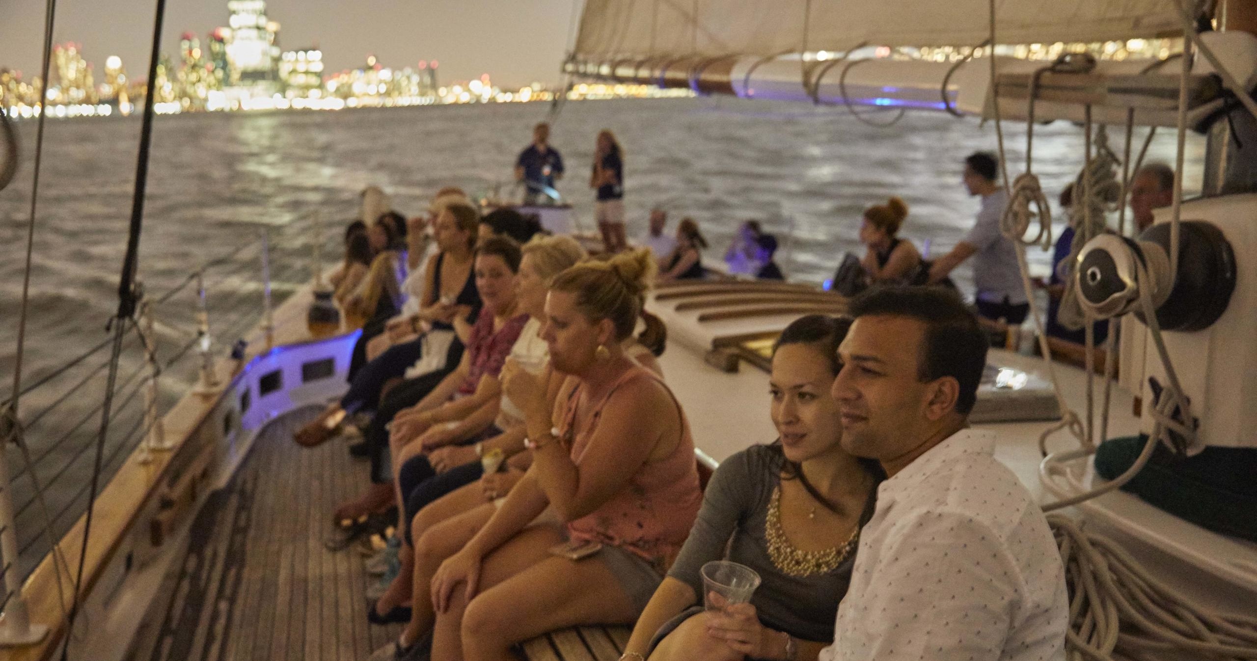 People sitting on a sailboat at night with city lights in the background.