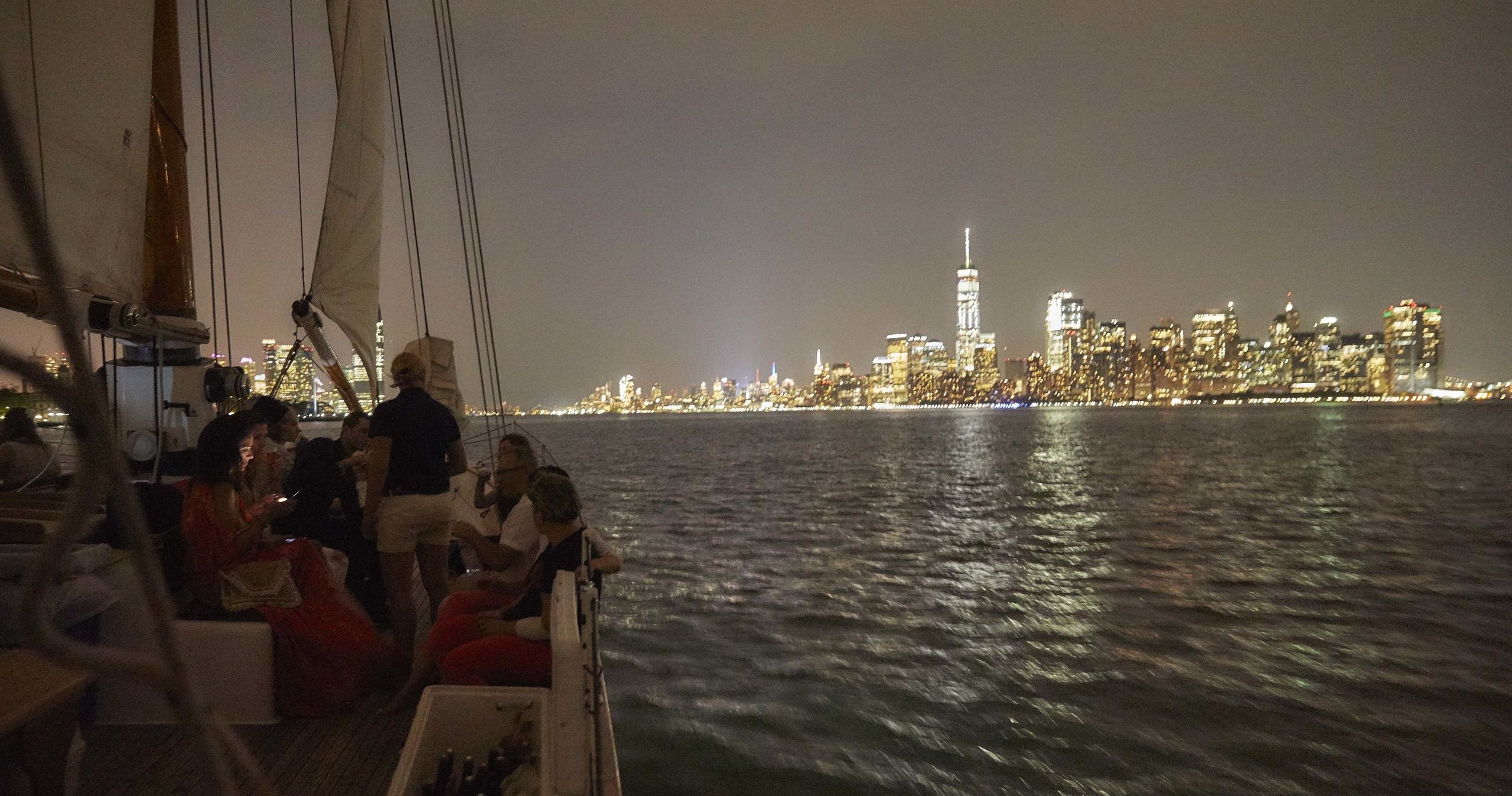 People on a boat at night with city skyline in the background.