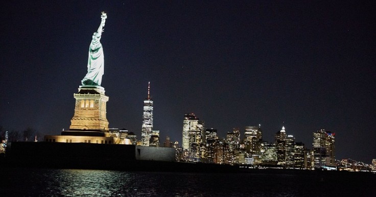 Statue of Liberty and New York City skyline at night, lights glowing.