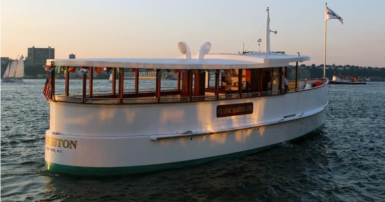 A classic white boat with flags sails on calm water at sunset.