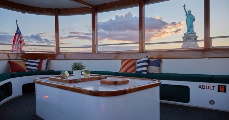 Cozy boat interior with Statue of Liberty and American flag in background.