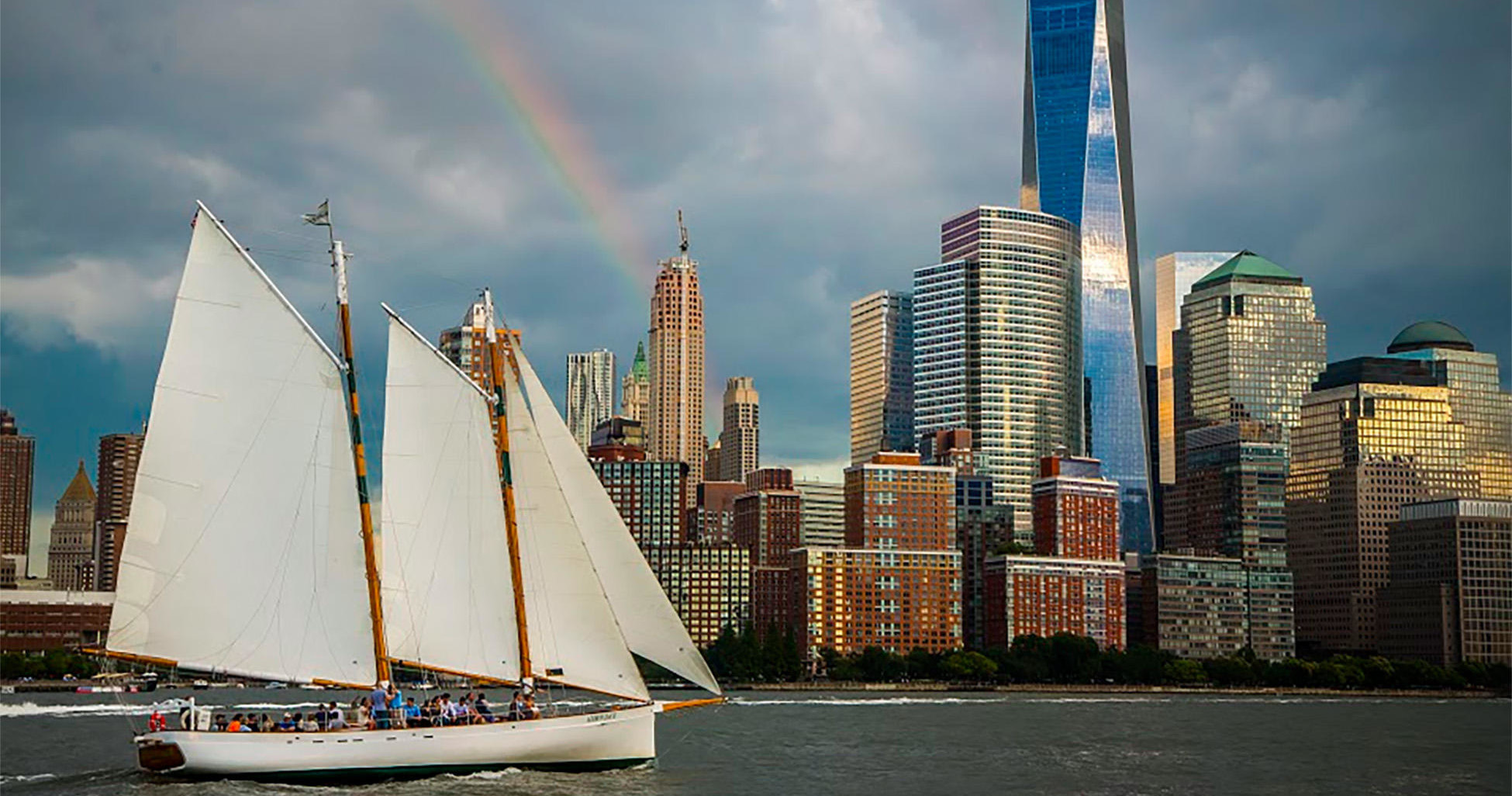 Sailboat on water with city skyline and rainbow in background.