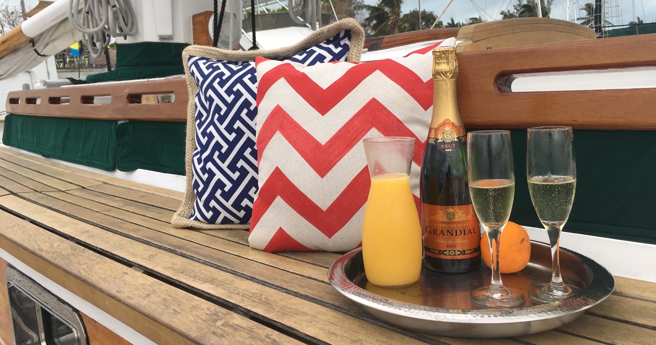 Sailboat deck with patterned pillows, tray holding champagne, orange juice, and glasses.