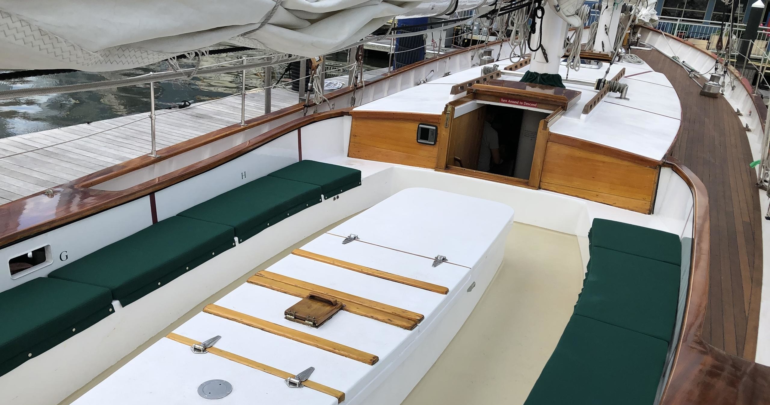 Sailboat deck with green cushioned seating, wooden accents, and open cabin entry.