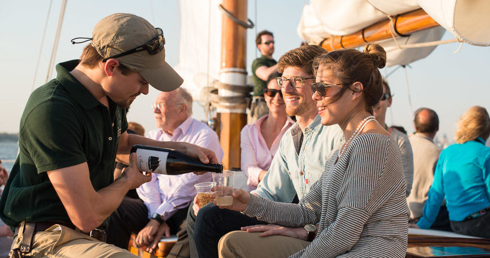 Person pouring wine for seated people on a sailboat.