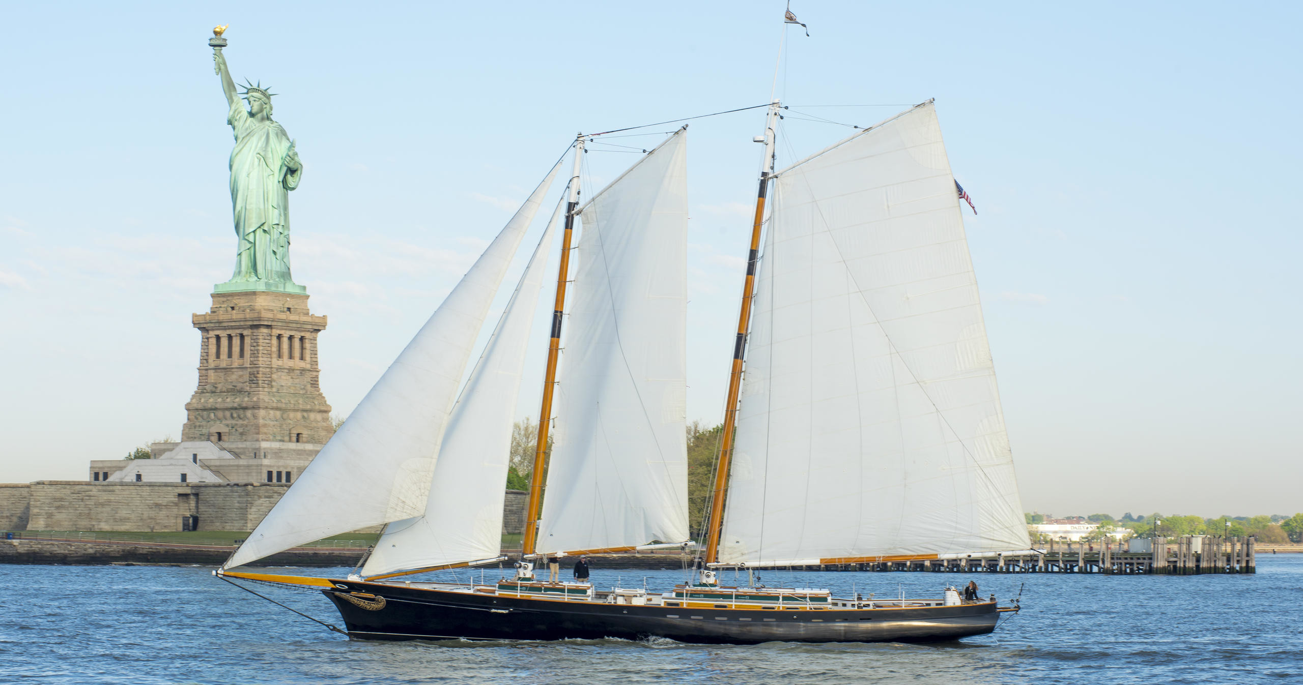 Sailboat in front of the Statue of Liberty on a clear day.