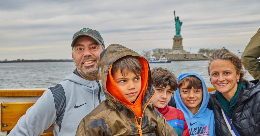 Smiling family posing on a boat with Statue of Liberty in background.