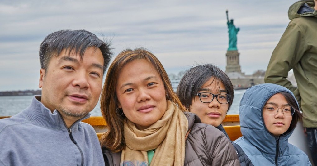 Family posing on a boat with the Statue of Liberty in the background.