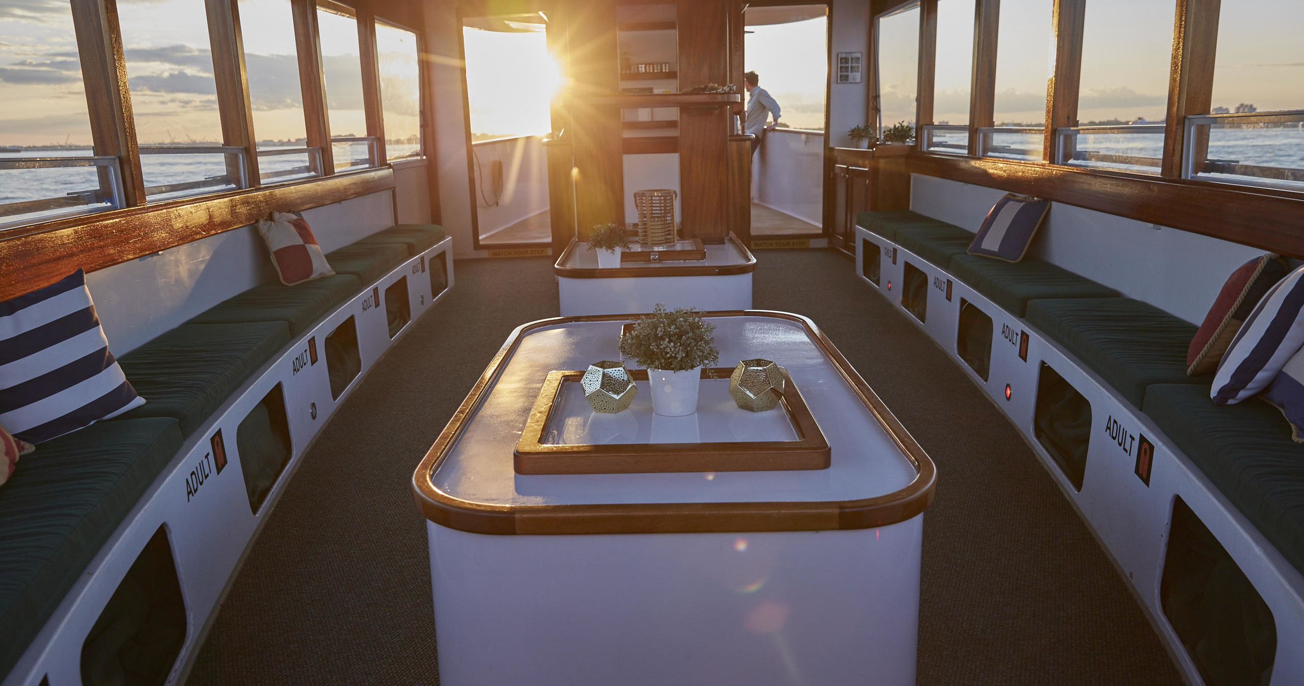 Boat interior with seating, sunlit windows, and a person at helm.