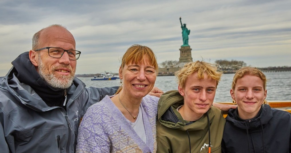 Family of four posing on a boat with the Statue of Liberty in the background.
