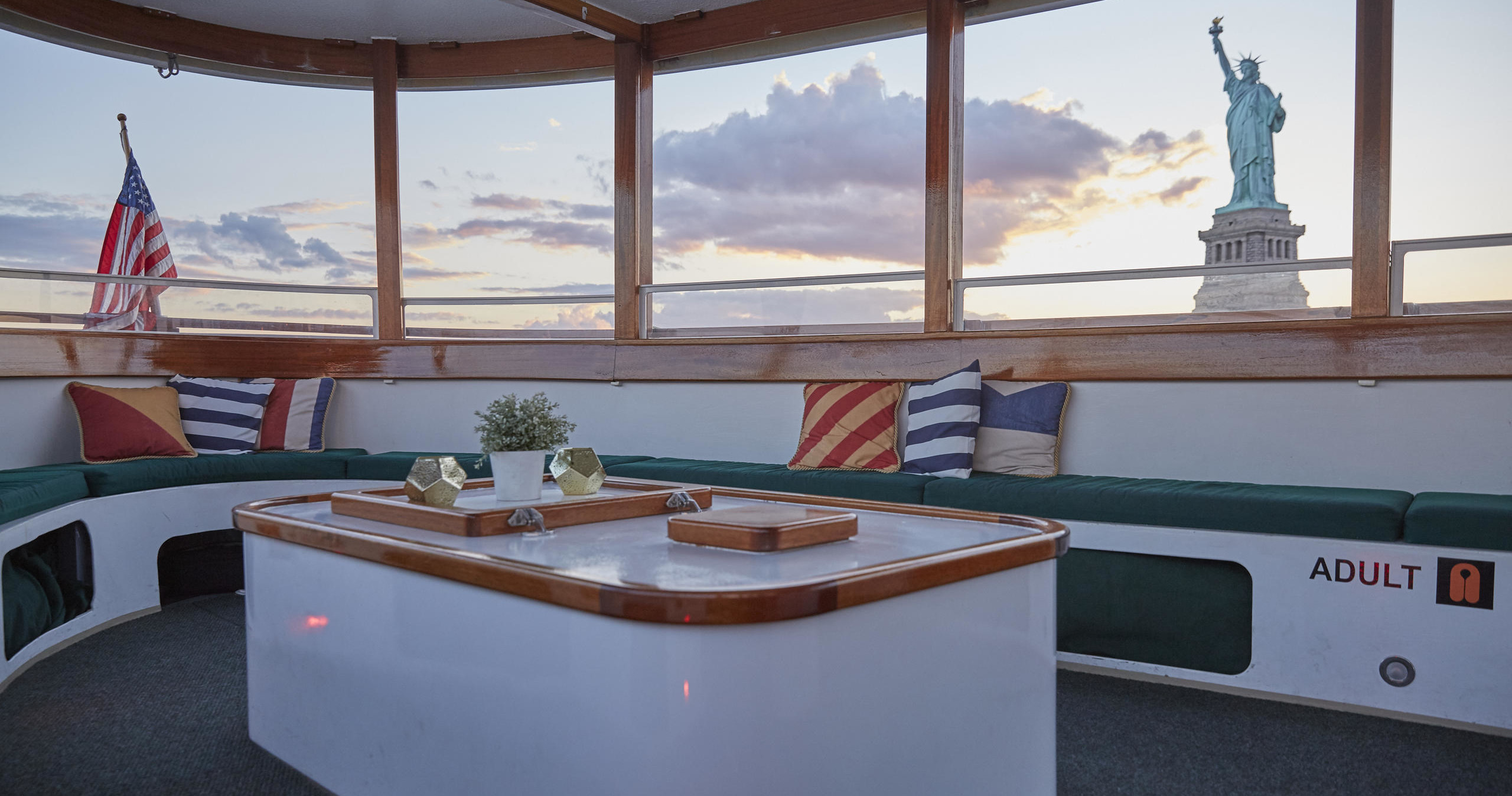 Boat interior with seating, U.S. flag, and Statue of Liberty view.