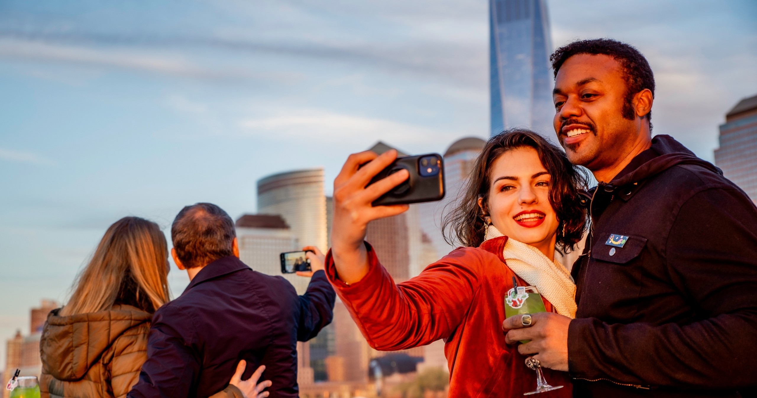 Two people taking a selfie with a city skyline in the background.