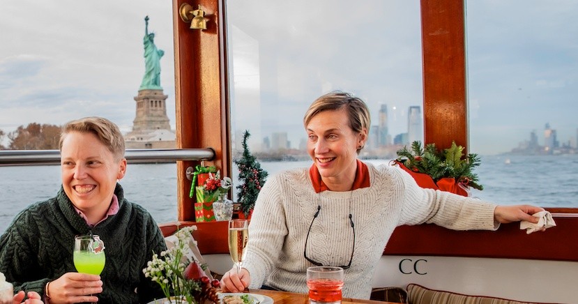 Two people smiling on a boat with the Statue of Liberty in the background.