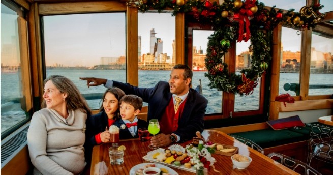 Family enjoying a holiday-themed boat ride with cityscape in the background.