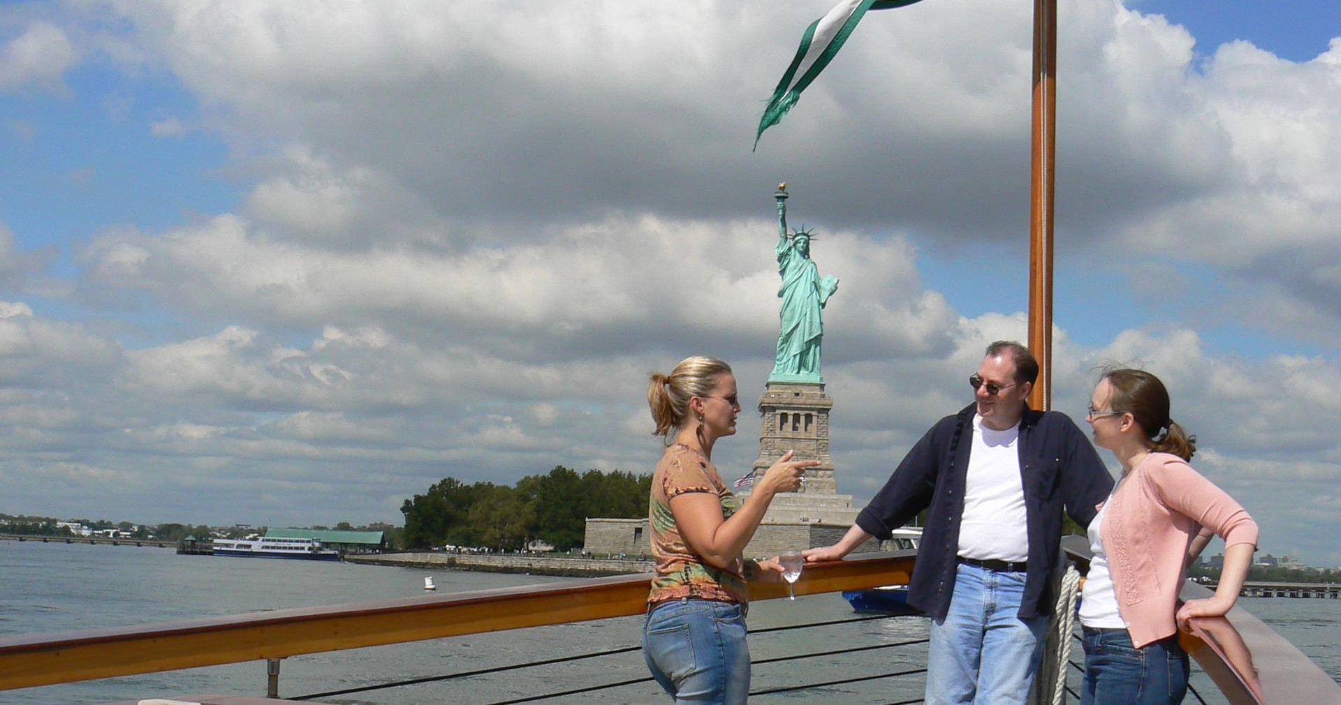 Three people on a boat near the Statue of Liberty, under a cloudy sky.