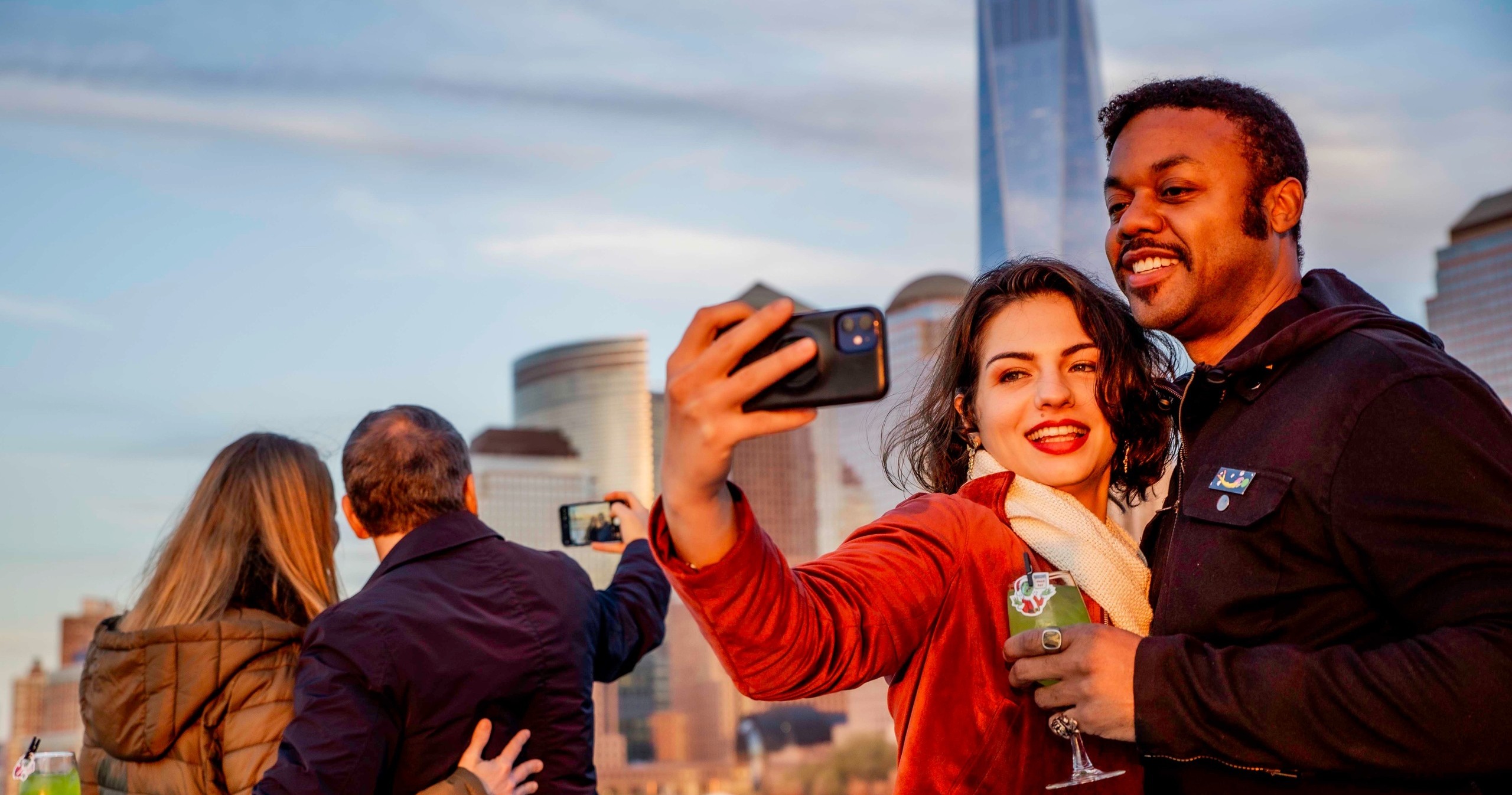 Couple taking selfie on rooftop with city skyline in background.