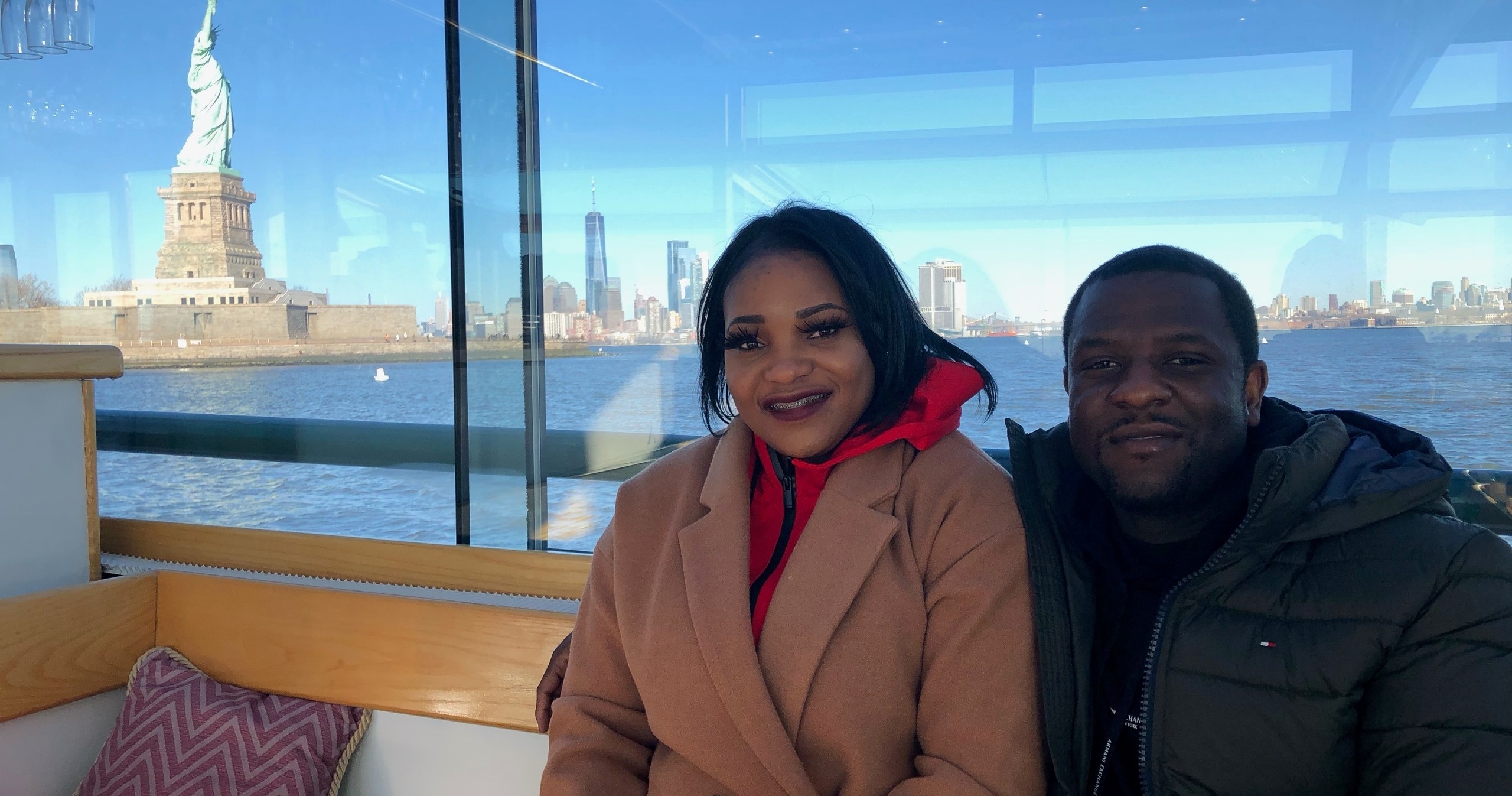 Two people smiling on a boat with the Statue of Liberty in the background.