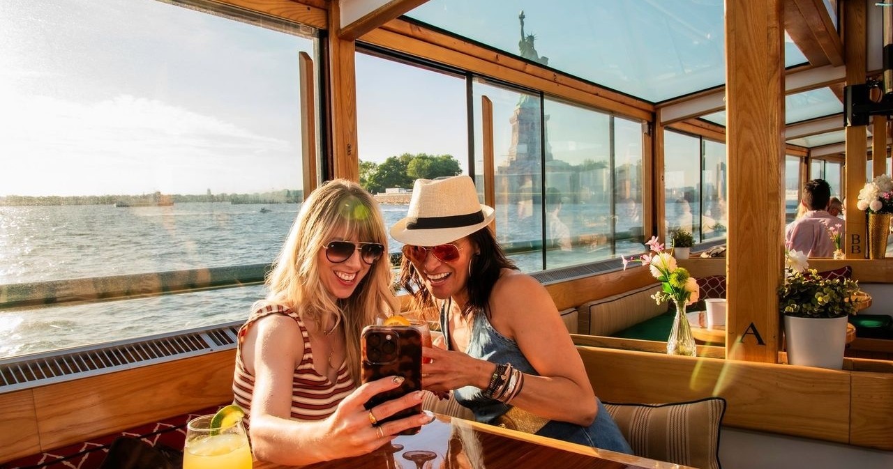 Two people on a boat taking a selfie with a waterfront view.