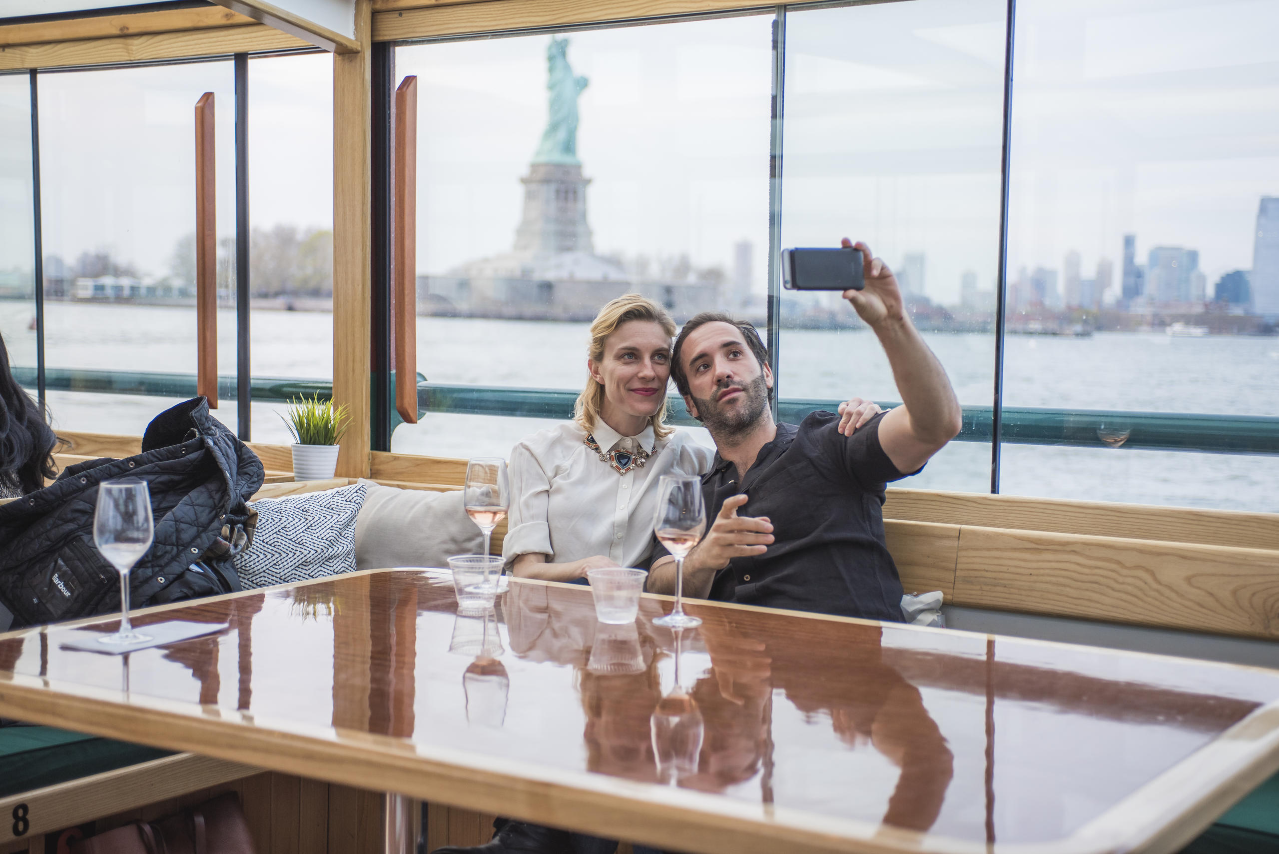 Couple taking a selfie on a boat with the Statue of Liberty in the background.
