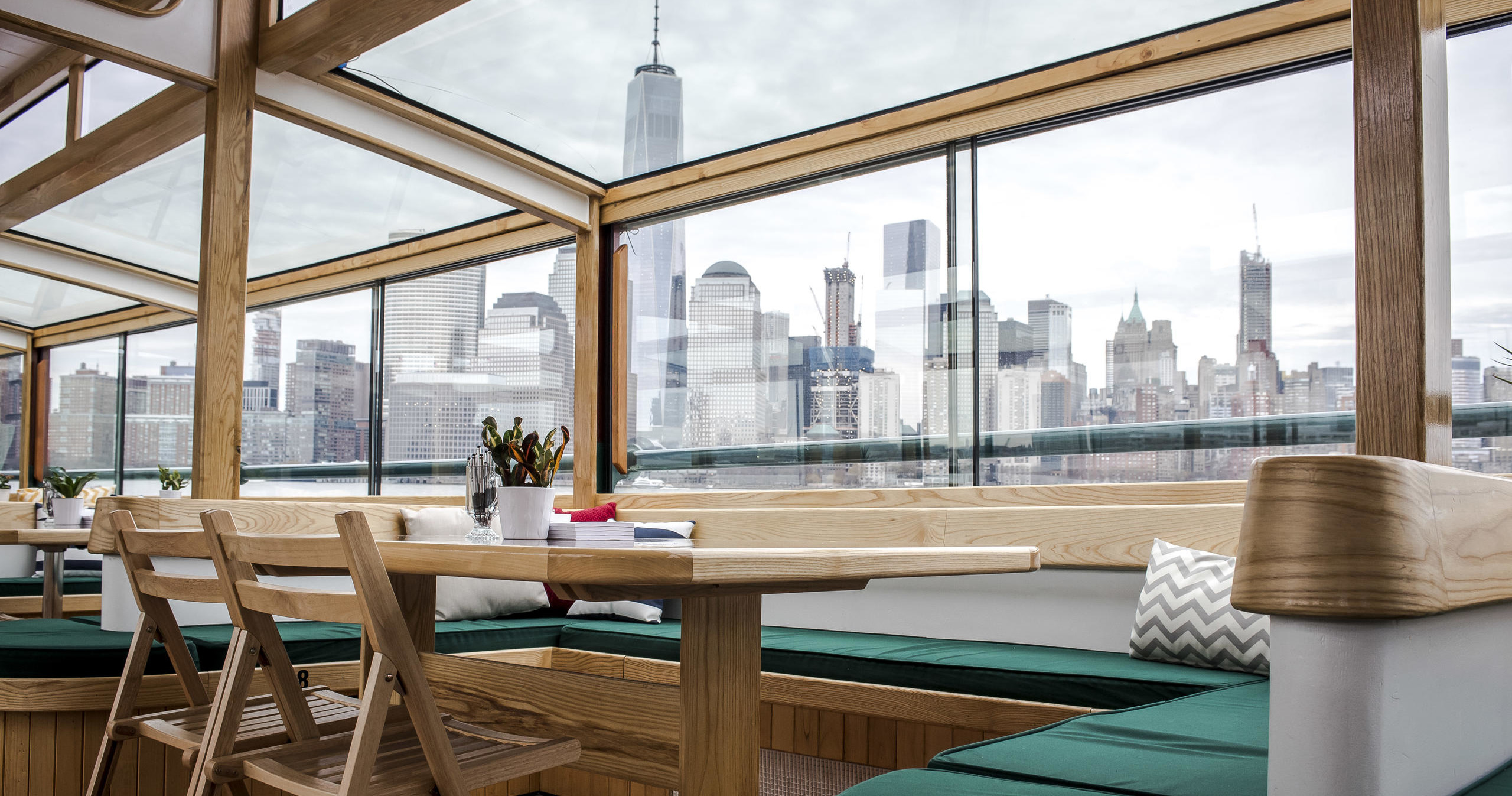 Indoor seating area with wooden table, skyline view through large windows.