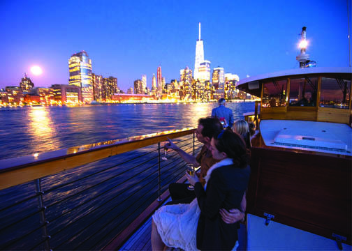 People on a boat at night, city skyline view, bright moon over water.