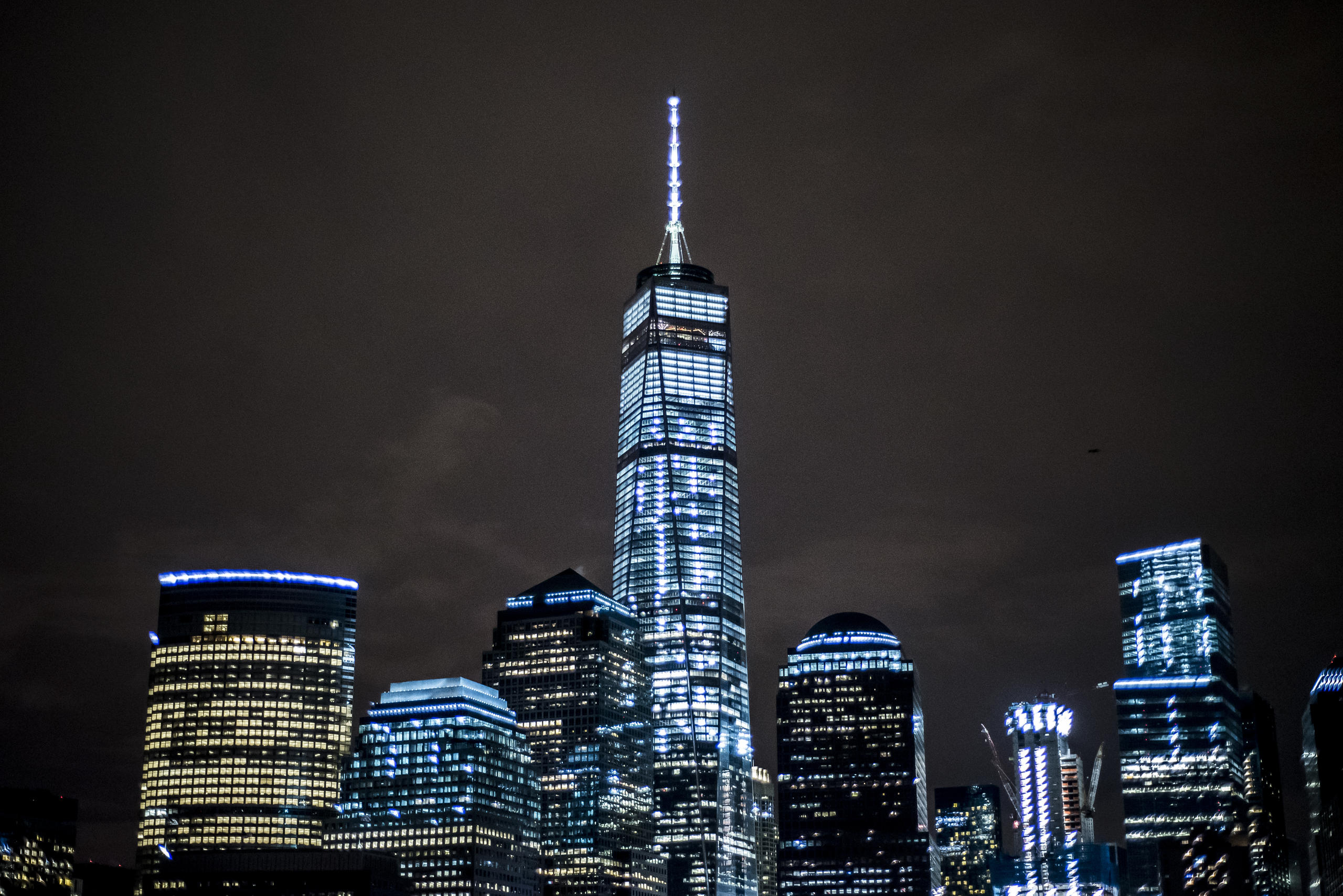 City skyline at night with tall, illuminated skyscraper in center.