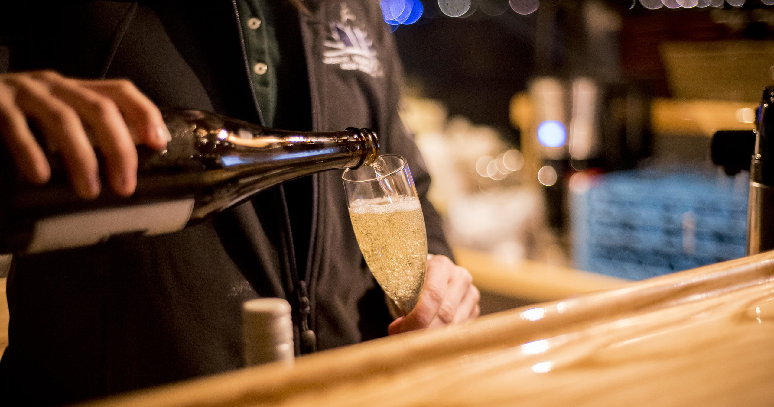Person pouring champagne into a glass at a bar.