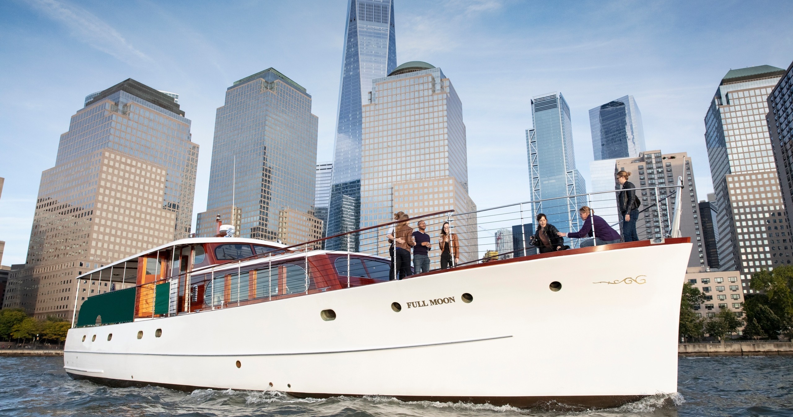 People standing on a yacht on a river with skyscrapers in the background.
