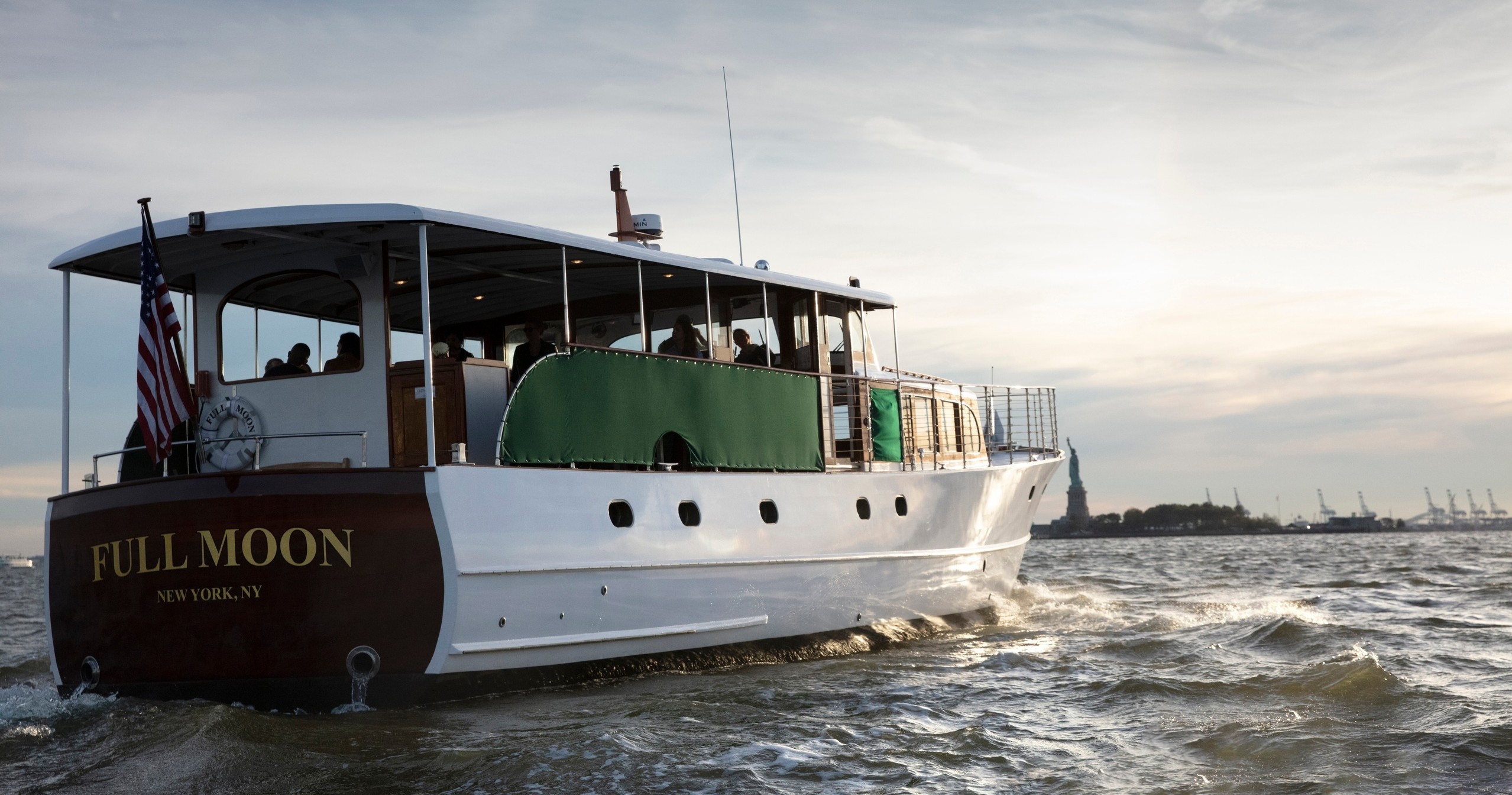 Boat named 'Full Moon' on water with the Statue of Liberty in the background.