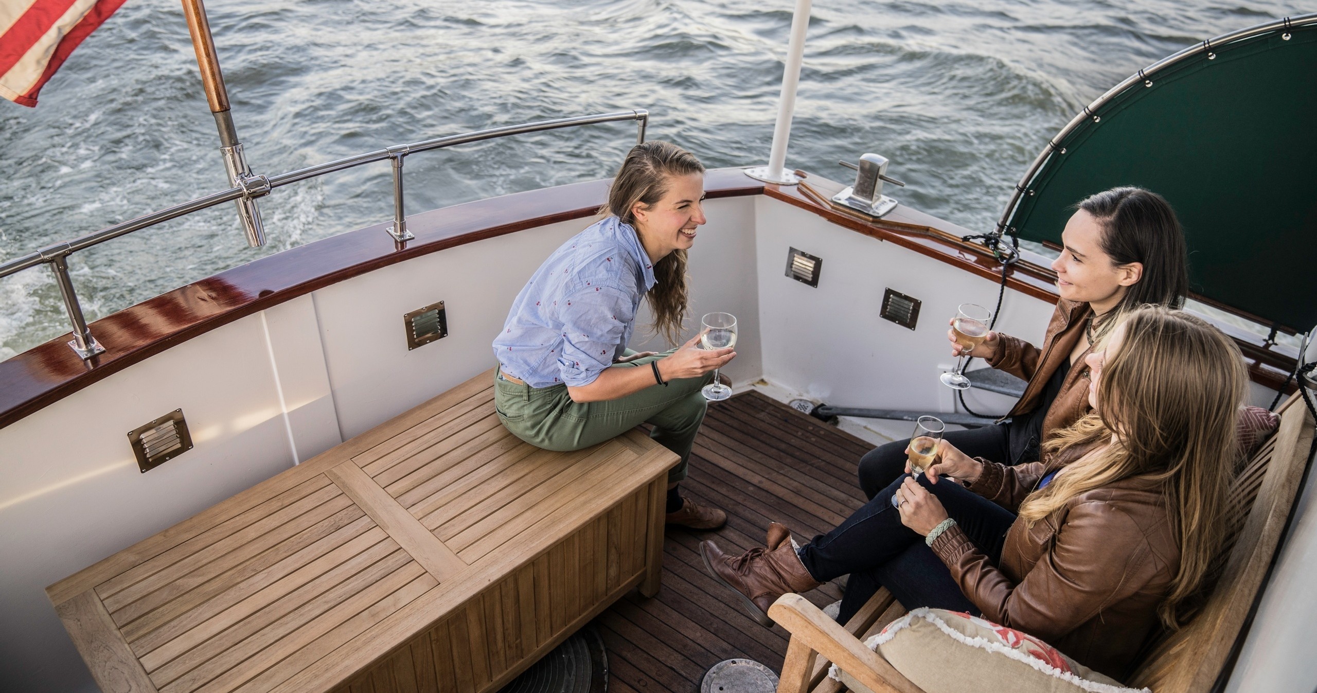 Three people on a boat laughing and holding drinks.