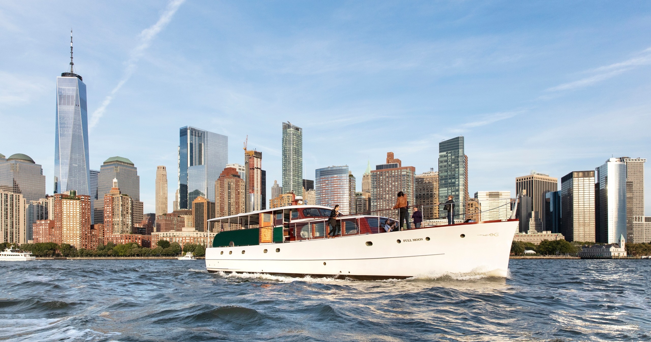 A boat sails on water with a city skyline, including skyscrapers, in the background.