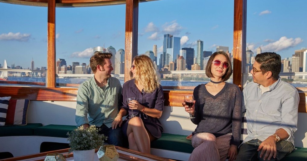 Four people sit on a boat with a city skyline in the background.