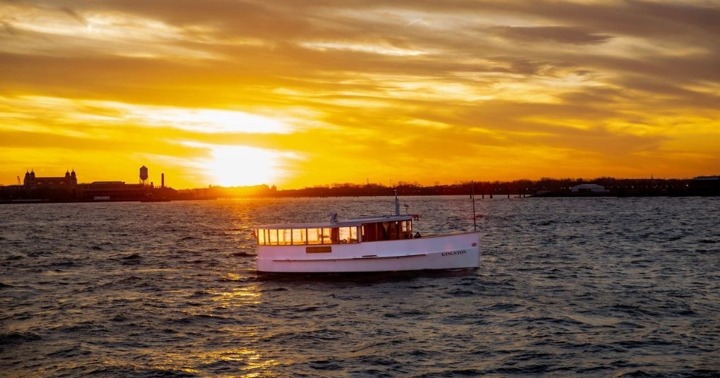 White boat on water with sunset and cloudy orange sky backdrop.