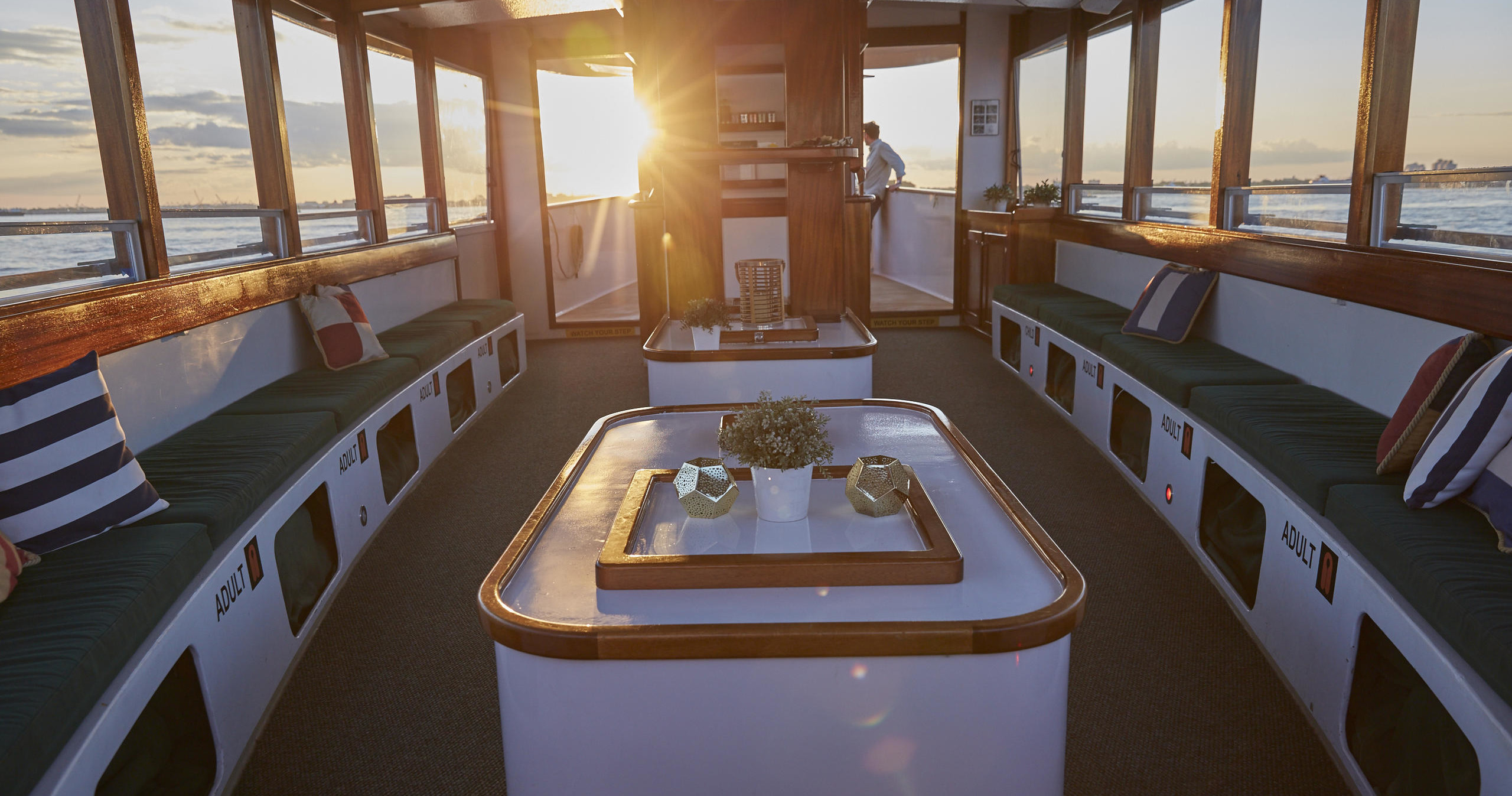 Sunlit boat interior with seating, cushions, and a central table.
