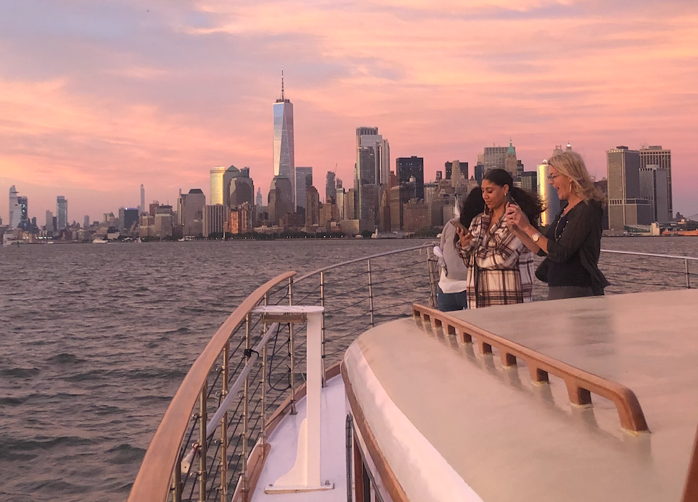 Three people on a boat with a city skyline and sunset in the background.