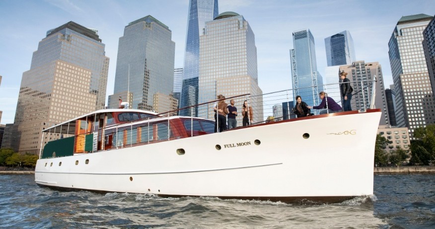 Boat with people on deck passing modern city skyscrapers.